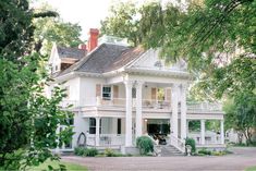 a large white house sitting on top of a lush green field next to tall trees