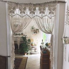 an open door with curtains and plants on the outside, in front of a living room