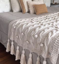 a white crocheted blanket with tassels on top of a bed in a bedroom