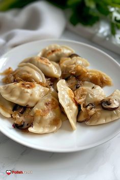 a white plate topped with dumplings covered in sauce and mushrooms on top of a table