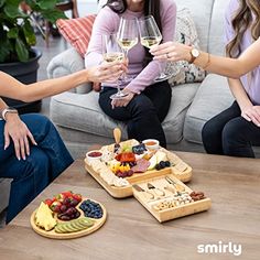 three women sitting on a couch holding glasses of wine and plates of food in front of them