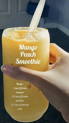 a hand holding a glass with mango peach smoothie in it's mouth and the words mango peach smoothie written on it