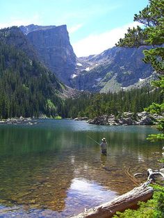 a man fishing in a lake surrounded by mountains