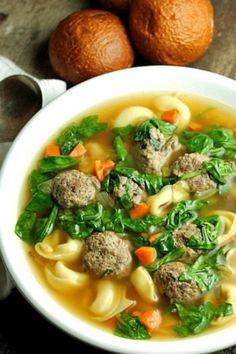 a white bowl filled with meatball soup next to two oranges on the table