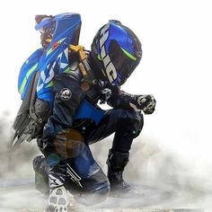 a man riding on the back of a motorcycle wearing a blue and black suit with his hands in his pockets