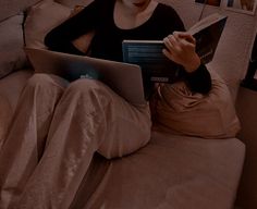 a woman sitting on a couch reading a book and looking at her laptop computer screen