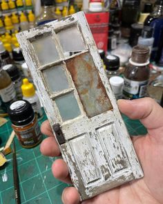 an old door is being held up by someone's hand in front of some paint bottles