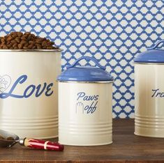 three white canisters with dog food in them on a table next to a blue and white wall