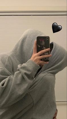 a person wearing a hoodie taking a selfie with a cell phone in their hand