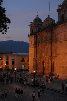 people are walking around in front of an old building at night with the lights on