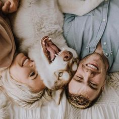 a man and woman laying on top of a bed next to a dog with its mouth open