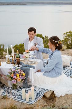 a man and woman sitting at a table with food in front of them on a blanket