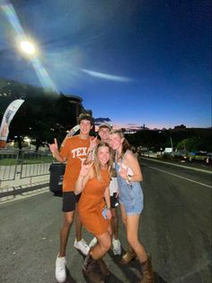 three young people posing for a photo on the side of the road at night time