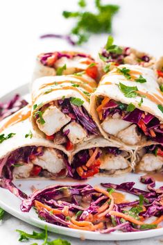 a white plate topped with two wraps filled with meat and veggies next to cilantro