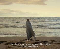 a person wrapped in a blanket standing on the beach looking out at the ocean and saying i love looking out at the ocean and imagine all the possibilities