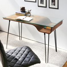 a glass desk with metal legs and a wooden table top in front of pictures on the wall