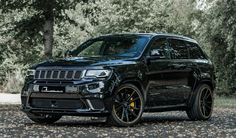 the black jeep is parked in front of some trees