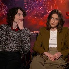 two women sitting next to each other with fireworks in the sky behind them and one woman holding her chin up