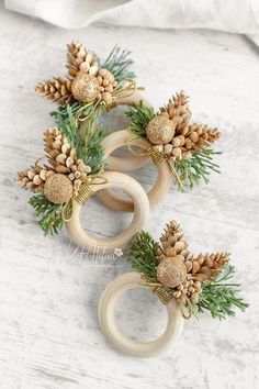 three wooden rings decorated with pine cones and gold balls are sitting on a white surface