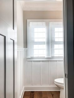 a white toilet sitting next to a window in a bathroom under a light fixture on a wooden floor