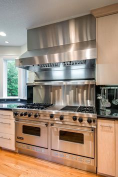 a stainless steel stove and oven in a kitchen with wood floors, cabinets and windows