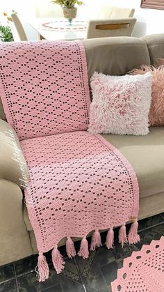 a pink crocheted afghan sitting on top of a couch next to two pillows