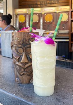 two tiki glasses sitting on top of a counter next to each other with flowers in them