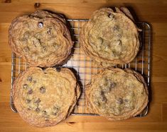 four chocolate chip cookies cooling on a wire rack in front of a wooden table top