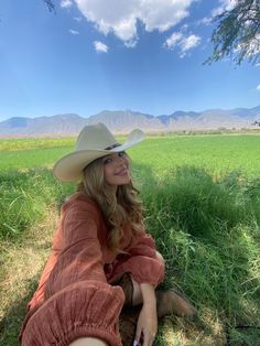 a woman sitting in the grass wearing a cowboy hat