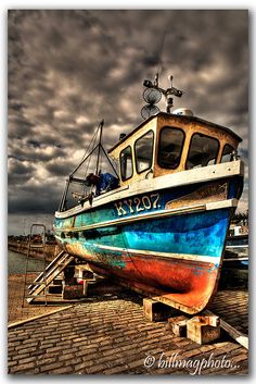 a boat sitting on top of a wooden dock next to the ocean under a cloudy sky