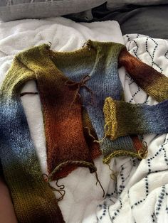 two knitted sweaters laying on top of a bed