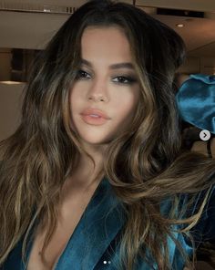 a woman with long brown hair wearing a blue suit and posing for the camera in front of a mirror