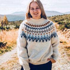 a woman standing on a dirt road wearing a sweater