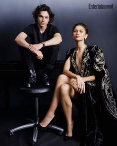 a man and woman sitting next to each other in front of a black background, posing for the camera