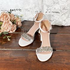 a pair of white high heeled shoes sitting on top of a wooden floor next to flowers