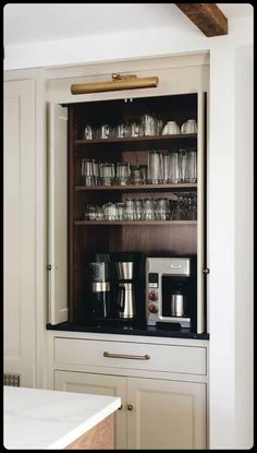 an open cabinet with many cups and glasses on the top, in front of a counter