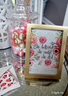 a table topped with pink and white flowers next to a glass jar filled with candy