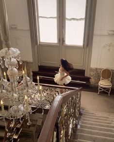 a woman in white dress standing on stairs next to chandelier