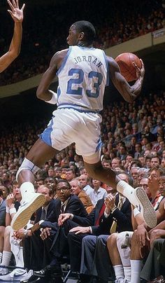 a basketball player jumping up to dunk the ball in front of an audience at a game