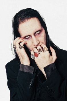 a man with long black hair holding his hands to his face and wearing rings on each hand