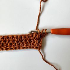 an orange crochet hook is hooked up to a knitting needle