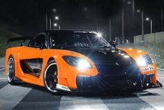 an orange sports car is driving down the road at night with its headlights turned on