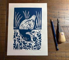 a blue and white drawing of a fish in the water next to some plants on a wooden table