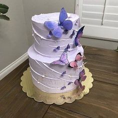 a three tiered cake with purple butterflies on the top and bottom, sitting on a wooden floor