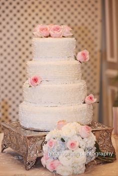 a white wedding cake with pink roses on top sits on a silver platter next to a bouquet of flowers