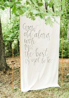 a white banner with writing on it sitting in the grass next to trees and leaves