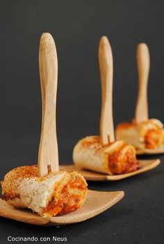 three pieces of pizza on wooden spoons with toothpicks sticking out of them