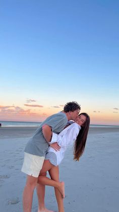 a man and woman kissing on the beach at sunset with their arms around each other