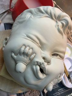 a clay sculpture of a laughing baby with paintbrushes in it's mouth