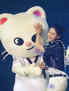 a woman is hugging a large white teddy bear on stage with one hand up to her face